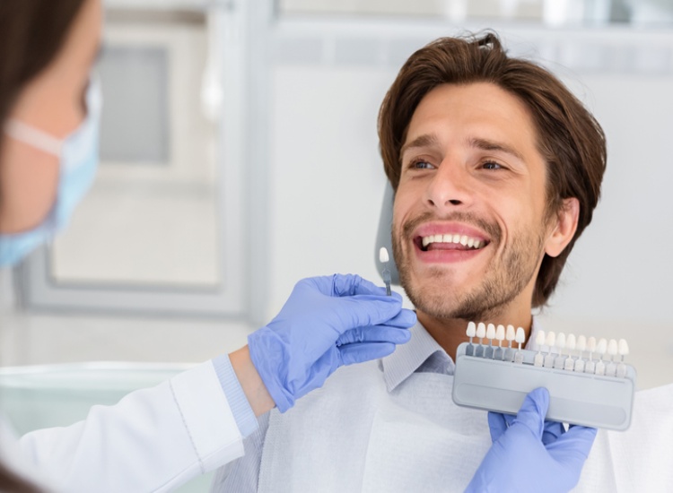 Dentist checks male patient's tooth shade with enamel scale at Mesa, AZ dental office.